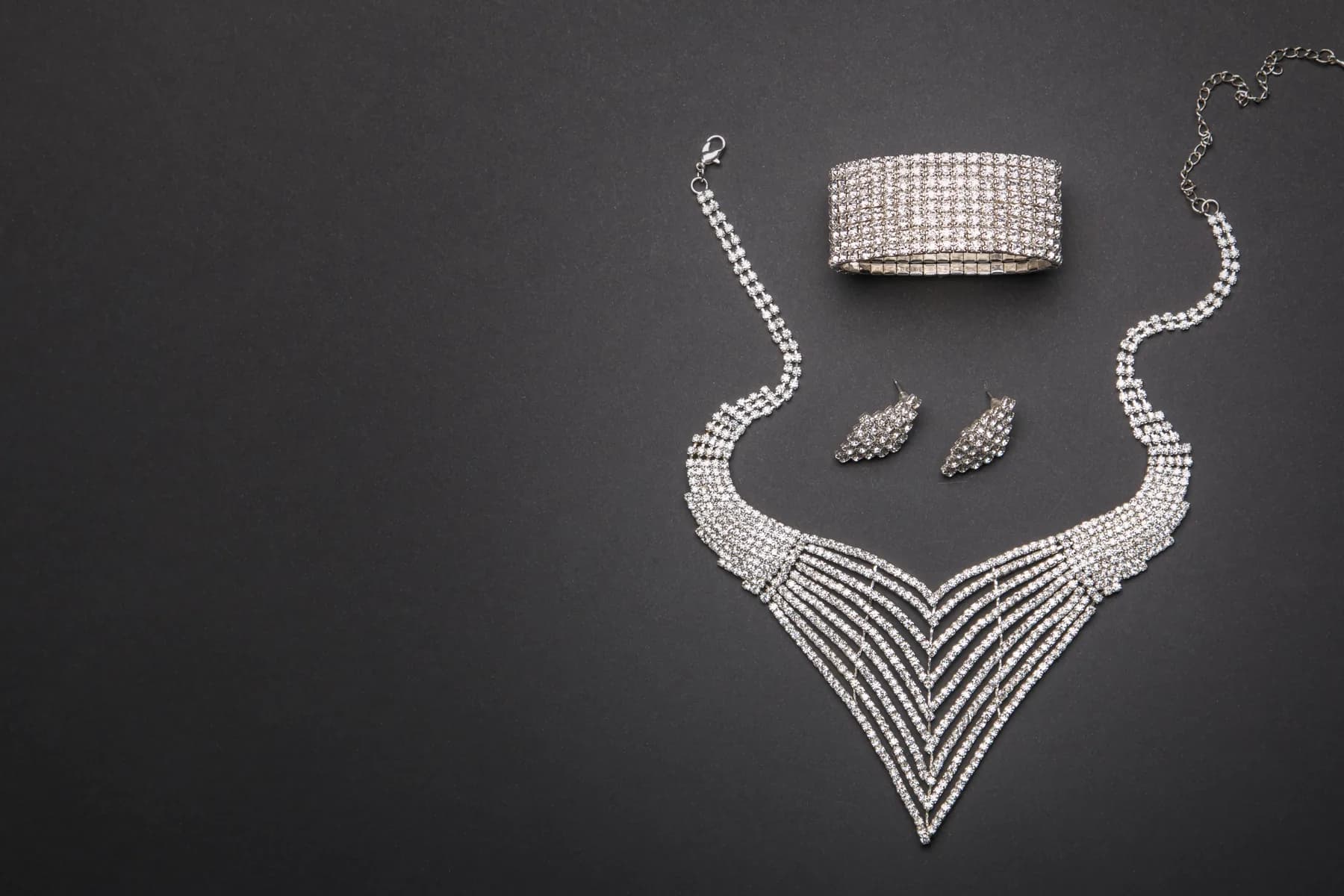 A diamond necklace, bracelet and earrings laid out on a dark ground
